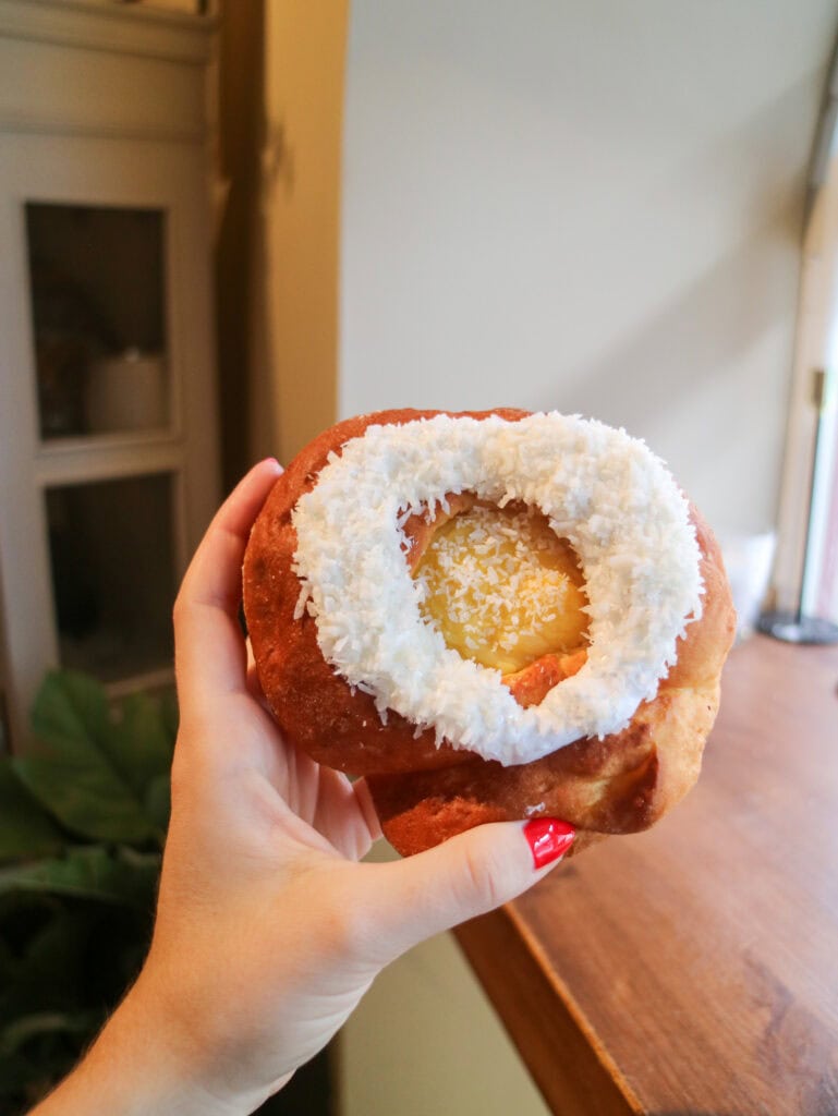 Close-up of a hand holding a coconut-filled doughnut with white shredded coconut.