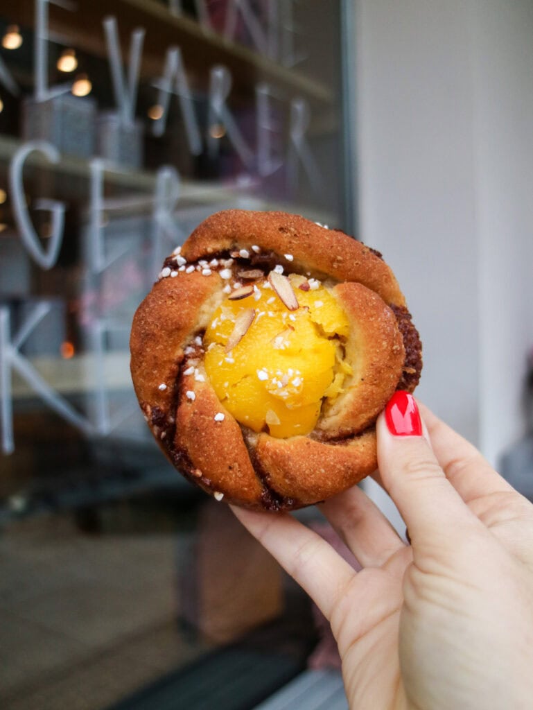 Close-up of a hand holding a Danish pastry with yellow custard filling.