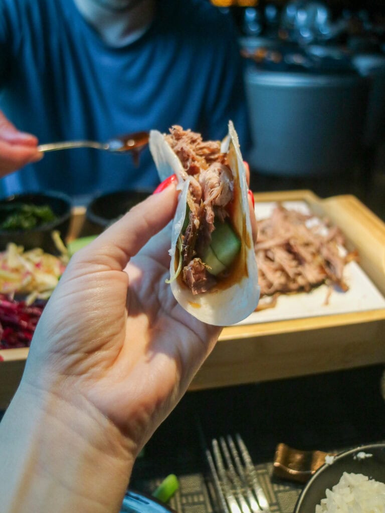 Close-up of a hand holding a taco with meat and vegetables in a restaurant setting.