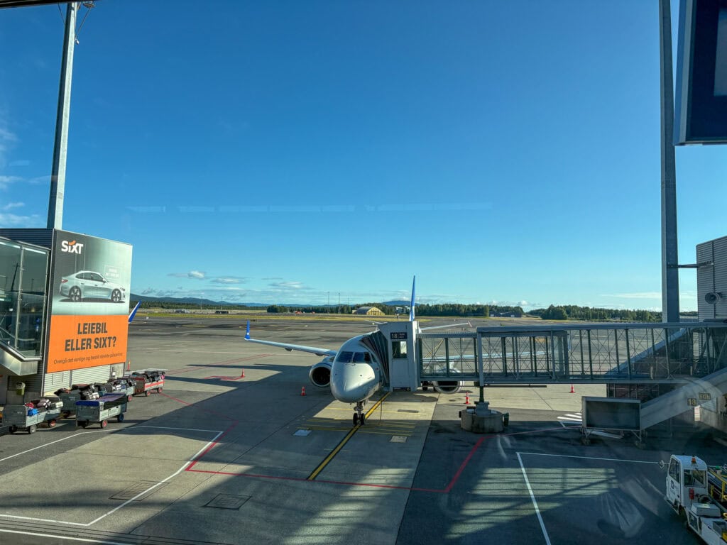 Small airplane parked at an airport gate with jet bridge and clear blue sky.