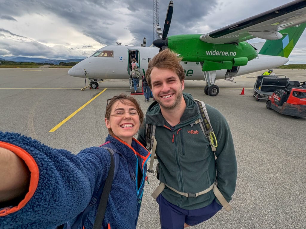 Travelers taking a selfie in front of a small airplane at the airport.