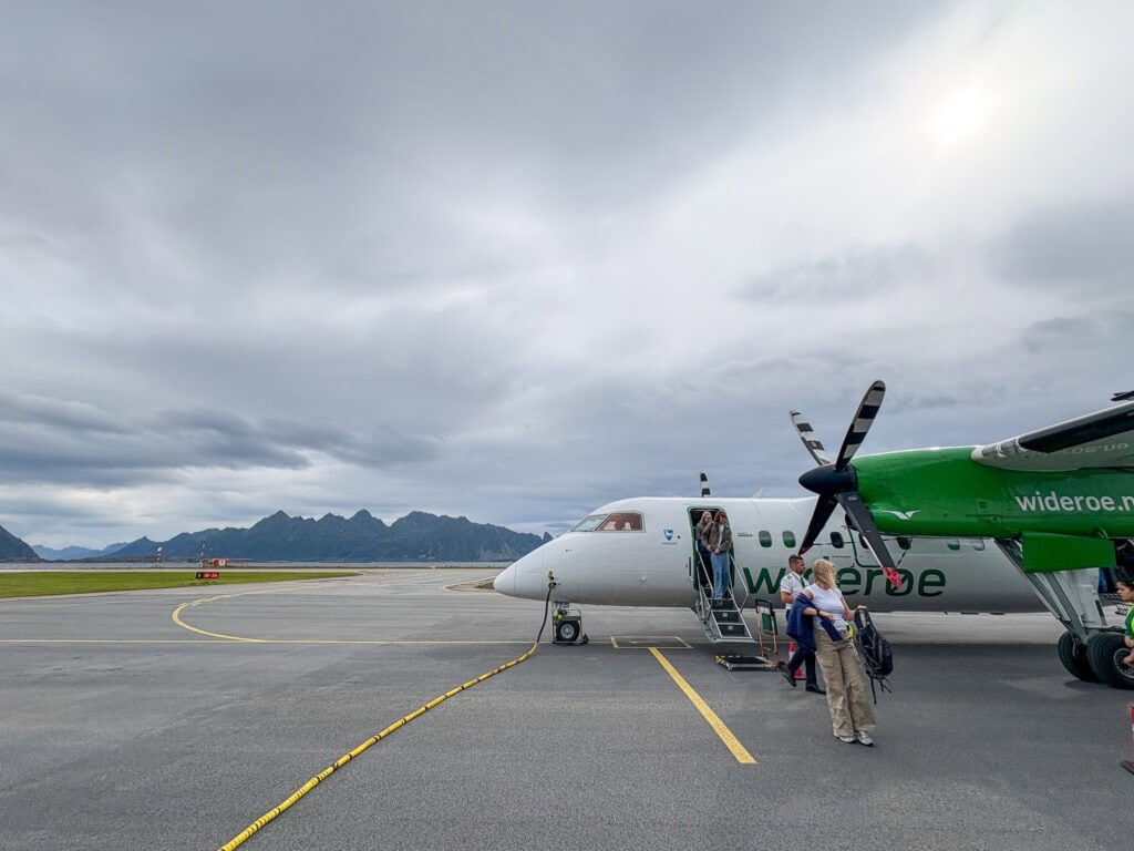 Small regional airplane on tarmac with passengers boarding under cloudy sky.