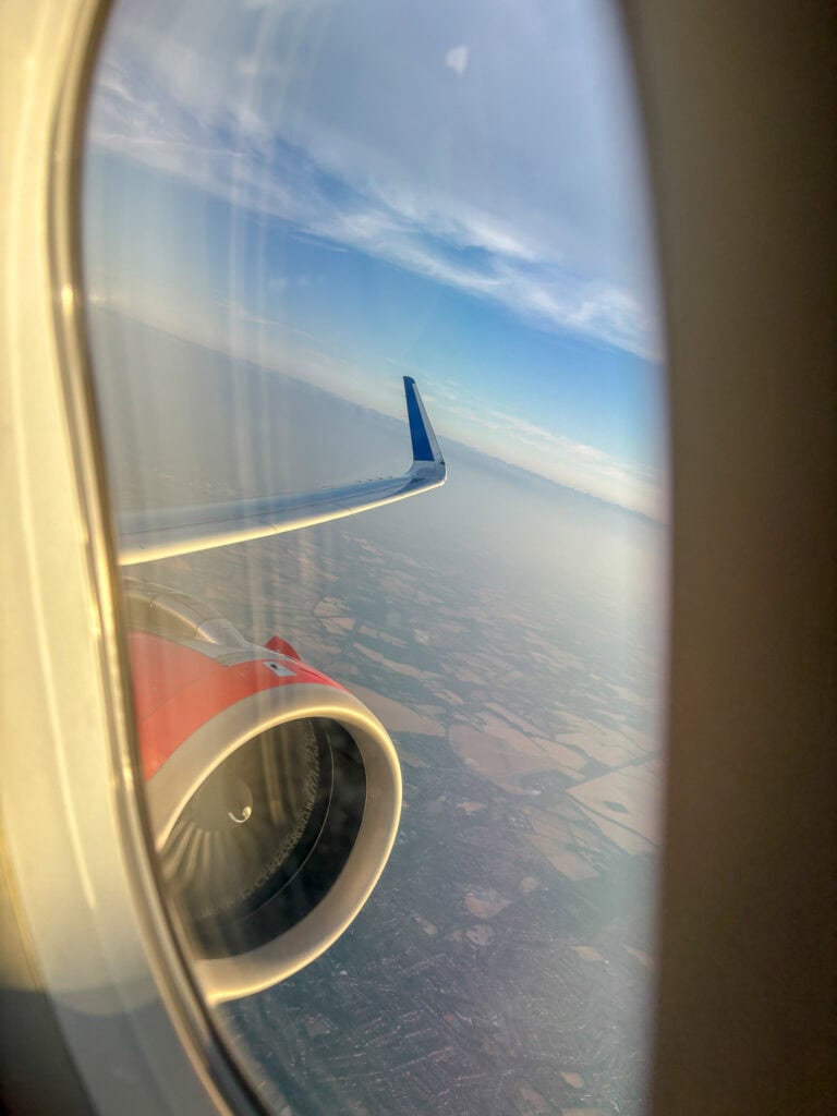 View from airplane window showing engine, wing, and landscape below.