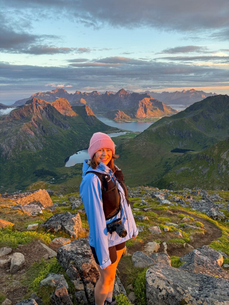 Woman hiking in Lofoten mountains during sunset with scenic landscape.