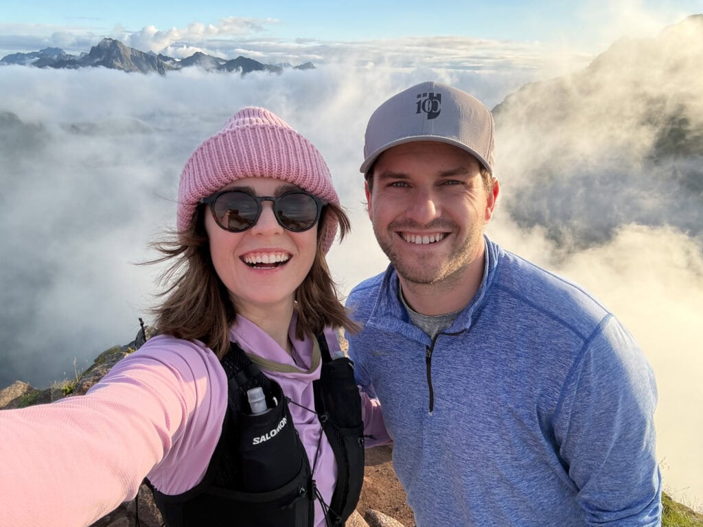 Smiling couple hiking in Lofoten mountains with clouds and peaks in background.