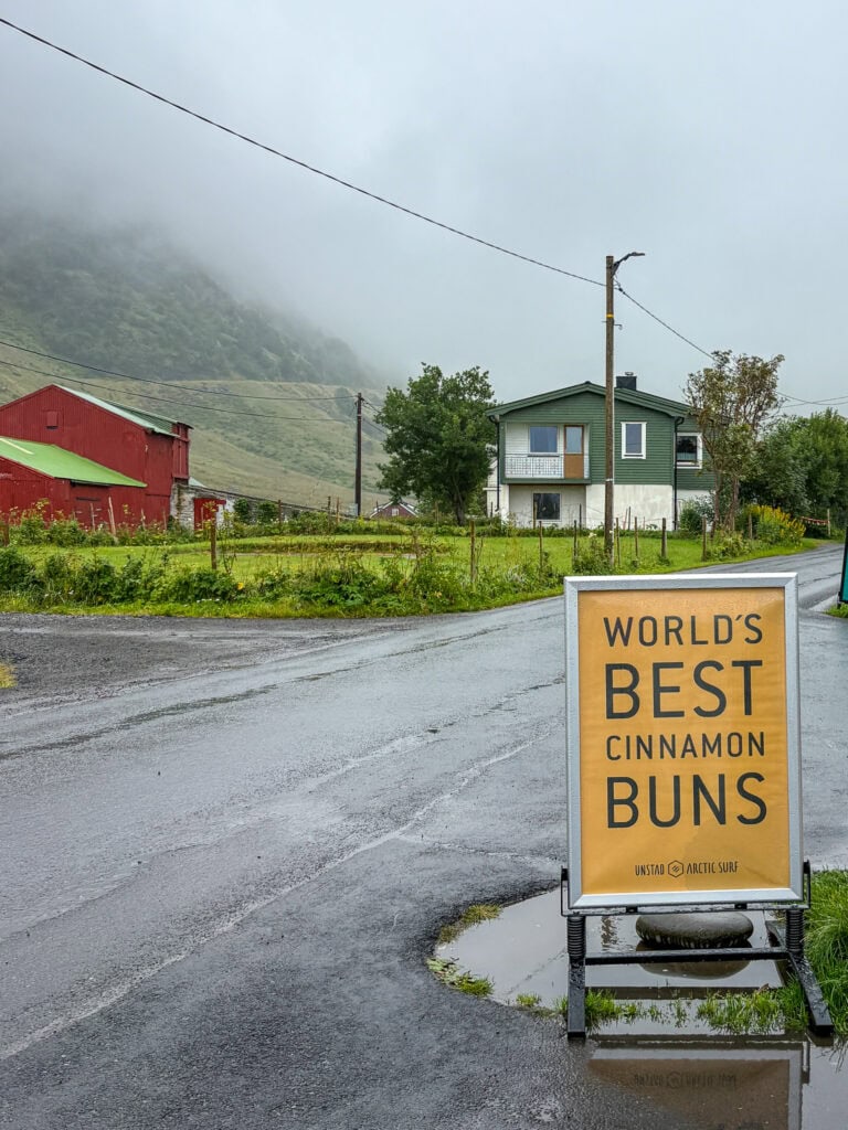 Sign advertising world's best cinnamon buns in a scenic, rainy village setting.