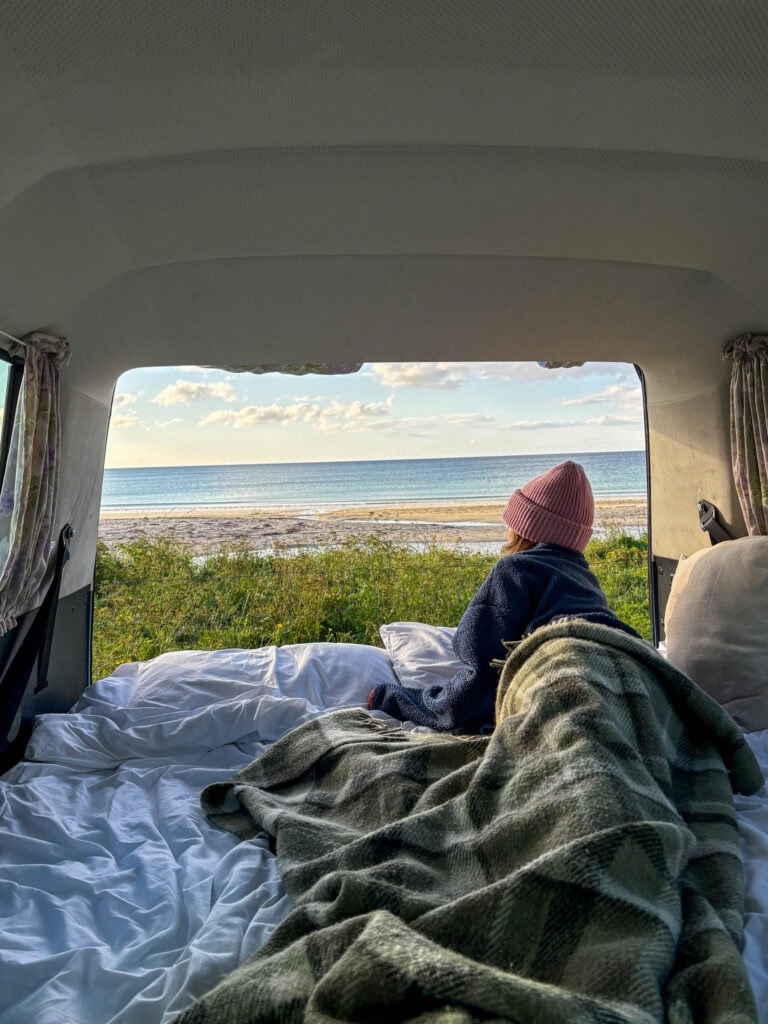 Person sitting in a camper van looking at the ocean view with a pink hat.