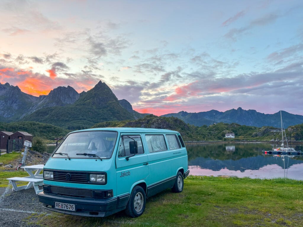 Scenic view of a blue van parked by a lake with mountains at sunset.