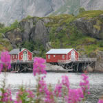 Colorful red houses on stilts by the water with mountains in the background.