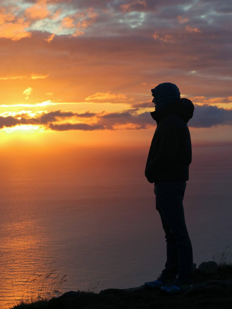 Person watching sunset over ocean in Lofoten, Norway during evening.