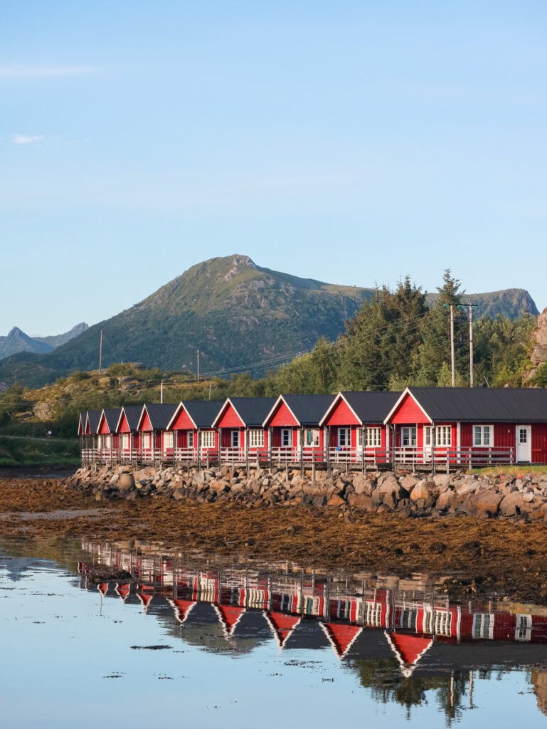 Colorful row of red houses along the shoreline with mountain backdrop in Lofoten, Norway.