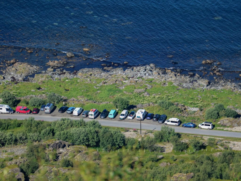 Scenic coastal road with parked cars and rocky shoreline in Lofoten, Norway.