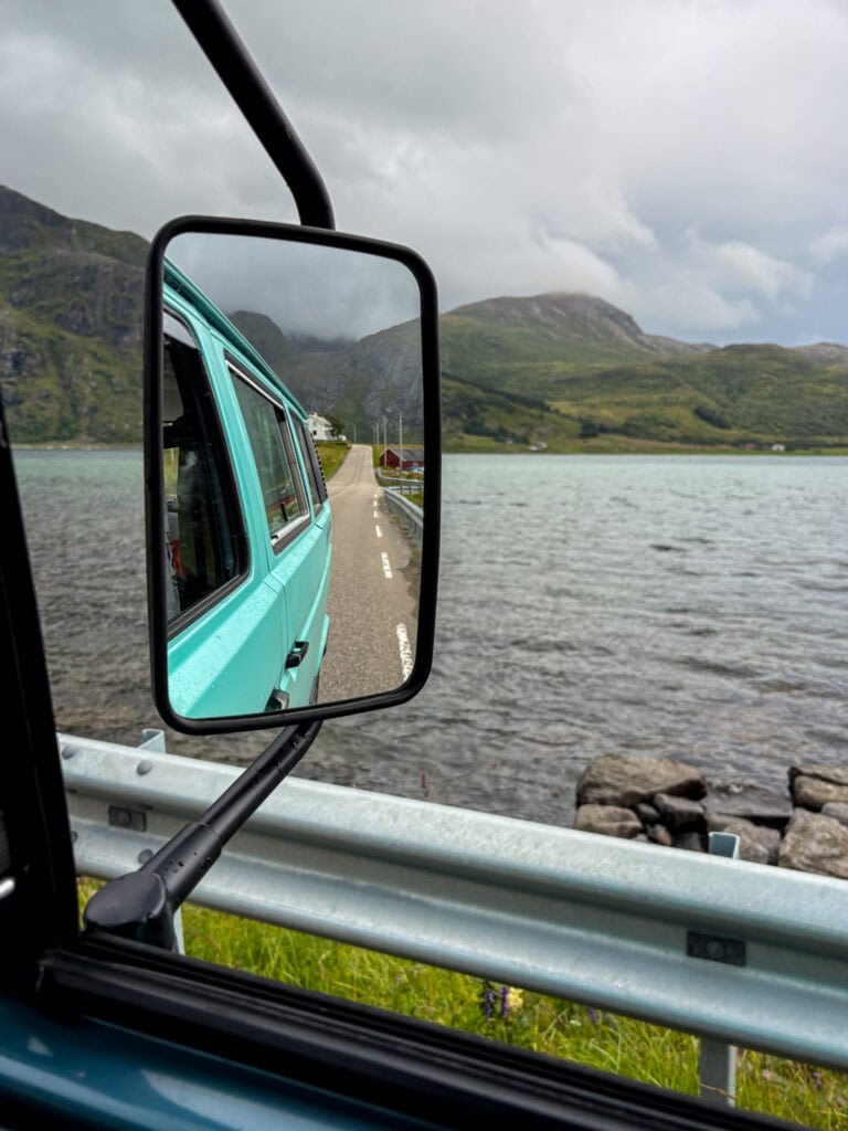 Scenic view of a turquoise van reflected in a side mirror by a lake in Lofoten, Norway.
