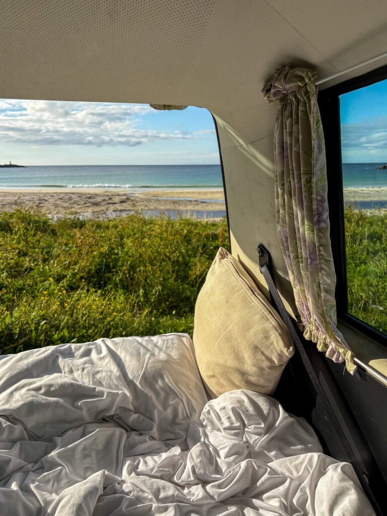 Cozy van interior with ocean view and open curtains, perfect for van life adventures.