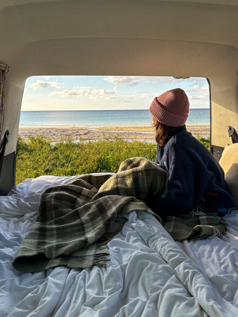 Woman in a pink beanie enjoying a beach view from a van.