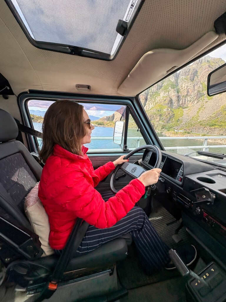 Woman driving a camper van through scenic fjord landscape in Lofoten, Norway.
