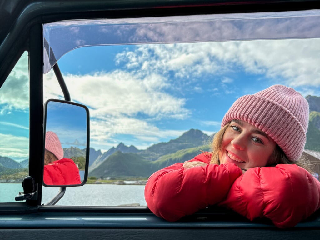 Woman in pink beanie and red jacket enjoying scenic mountain view from van window.