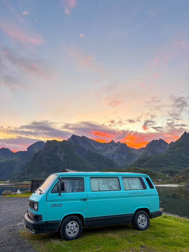 Vibrant blue camper van parked near a mountain lake at sunset in Lofoten.