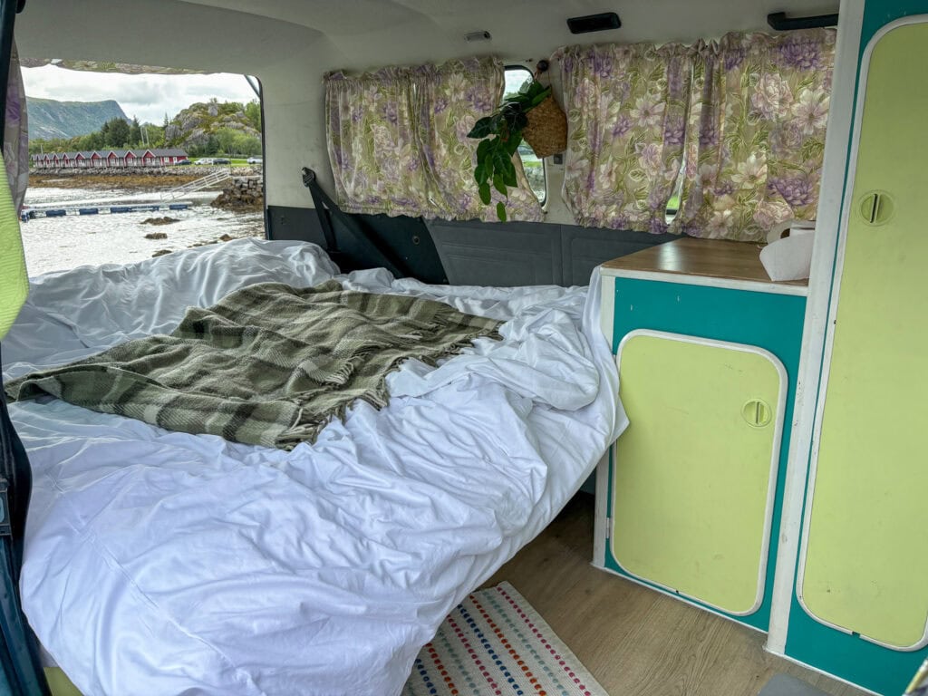 Cozy van interior with bed, floral curtains, and scenic view outside.