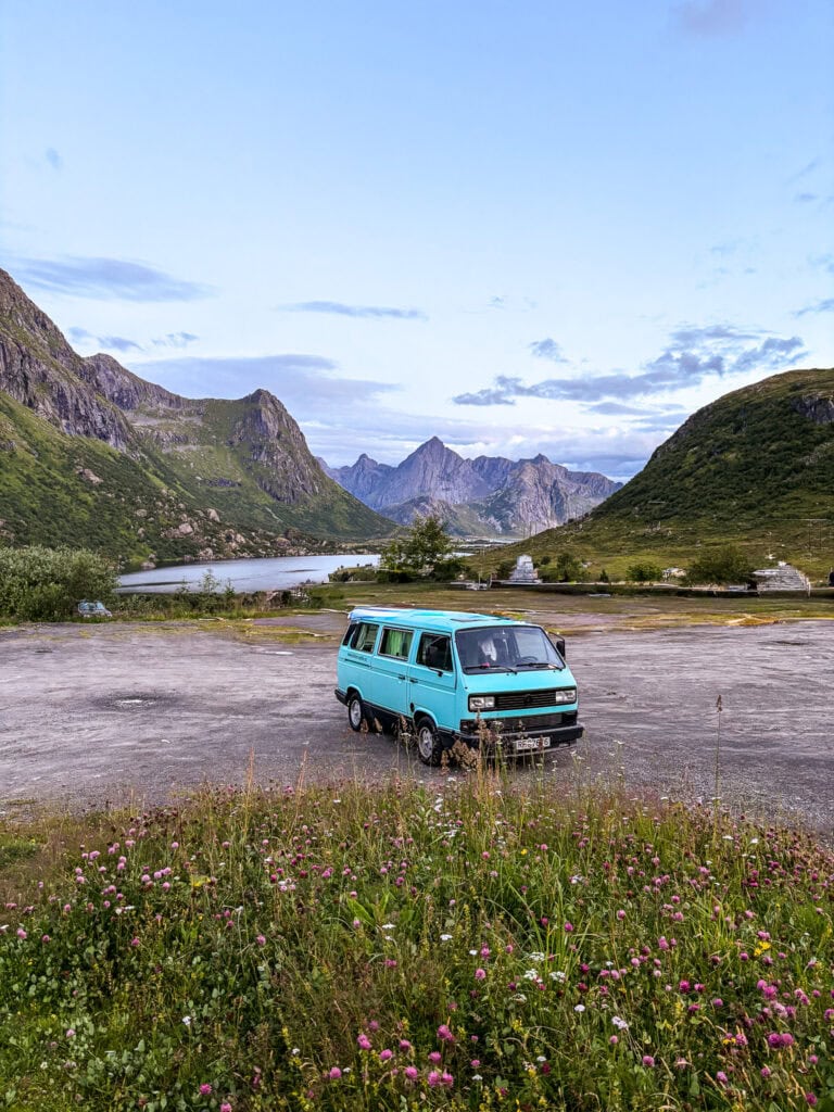 Vintage teal van parked in scenic Lofoten mountain landscape with wildflowers.