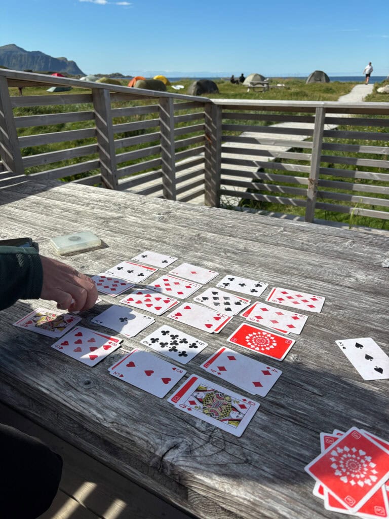 Playing cards spread out on a wooden table outdoors with scenic mountain and ocean view.