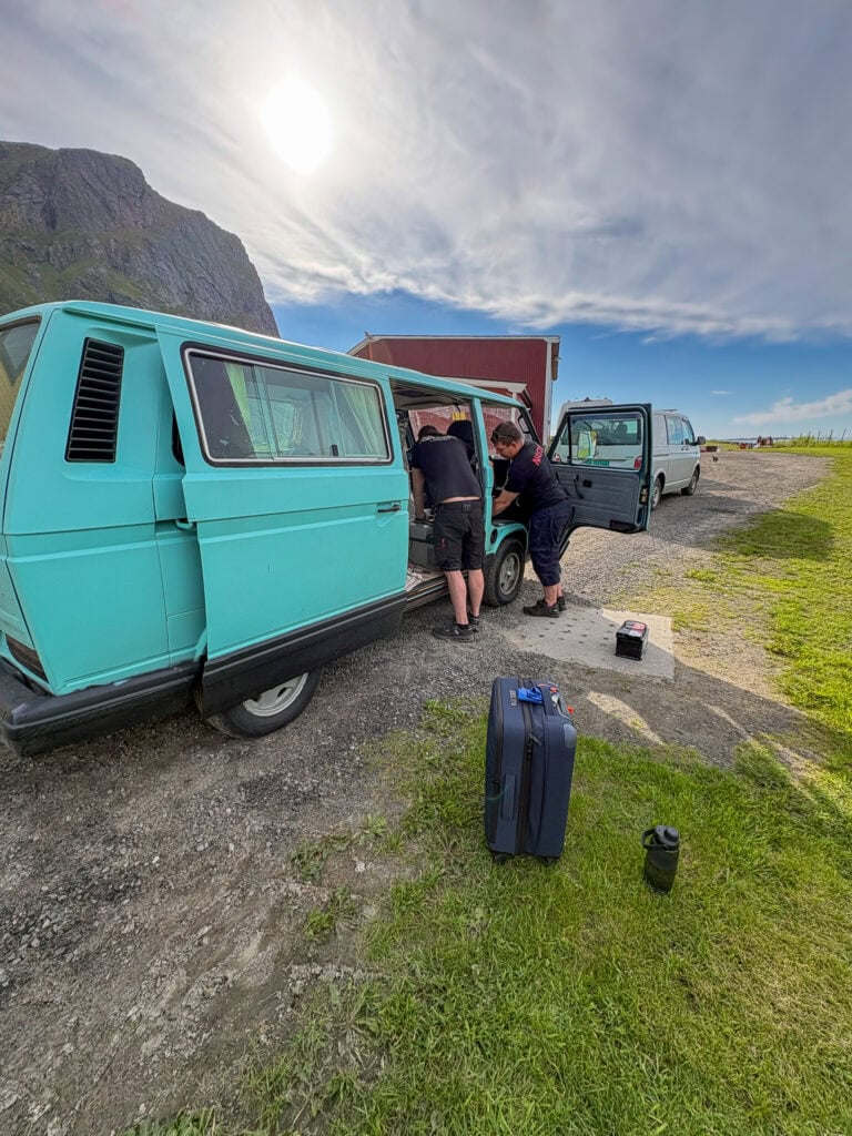People working on a vintage camper van in a scenic outdoor setting.