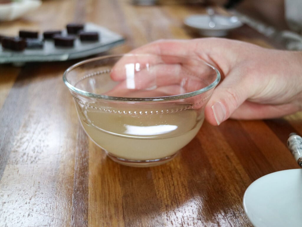Hand holding a glass bowl with traditional Korean rice wine, on a wooden table.