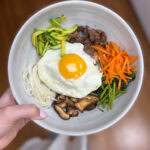 Korean bibimbap with vegetables, beef, egg, and mushrooms in a bowl.