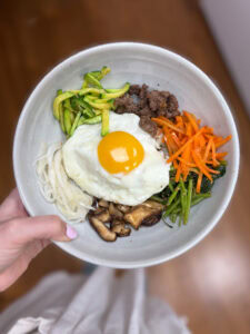Korean bibimbap with vegetables, beef, egg, and mushrooms in a bowl.