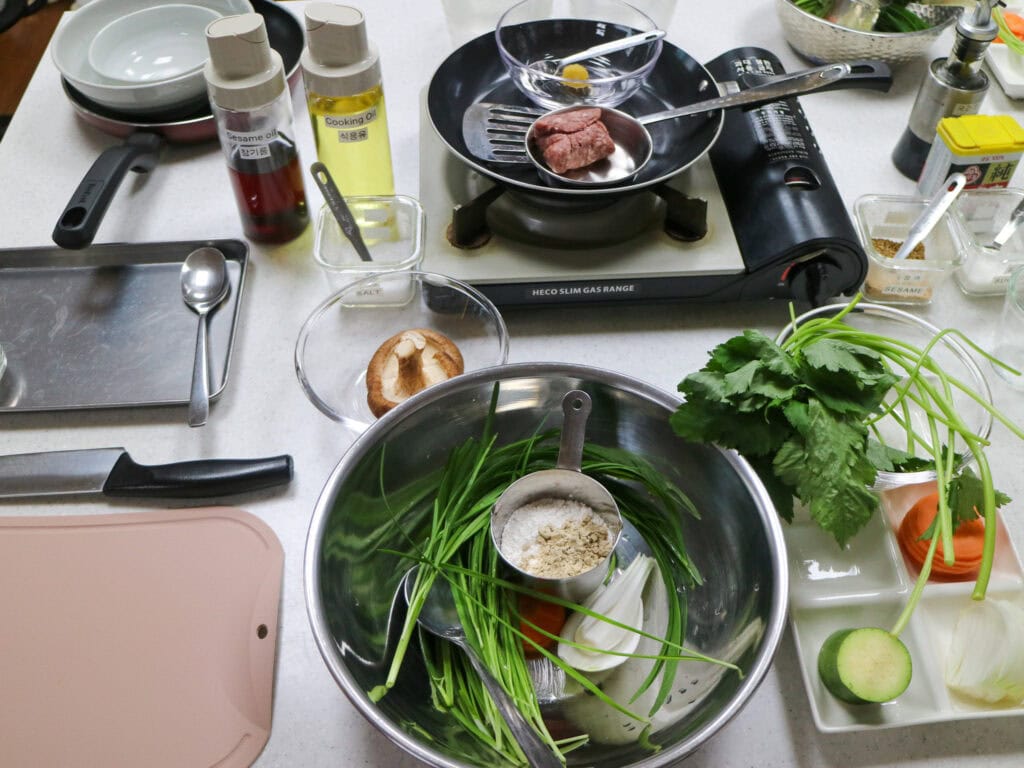 Cooking class setup with fresh vegetables, herbs, and cooking tools on a kitchen counter.