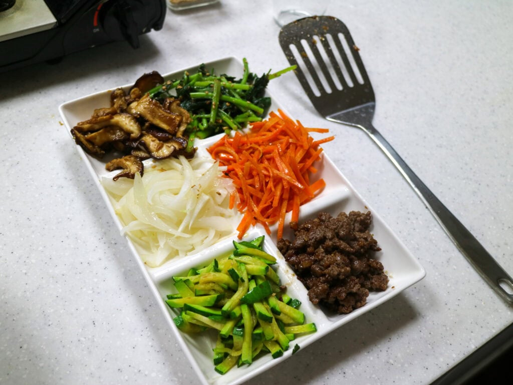 Assorted Korean side dishes on a white rectangular plate for cooking class.