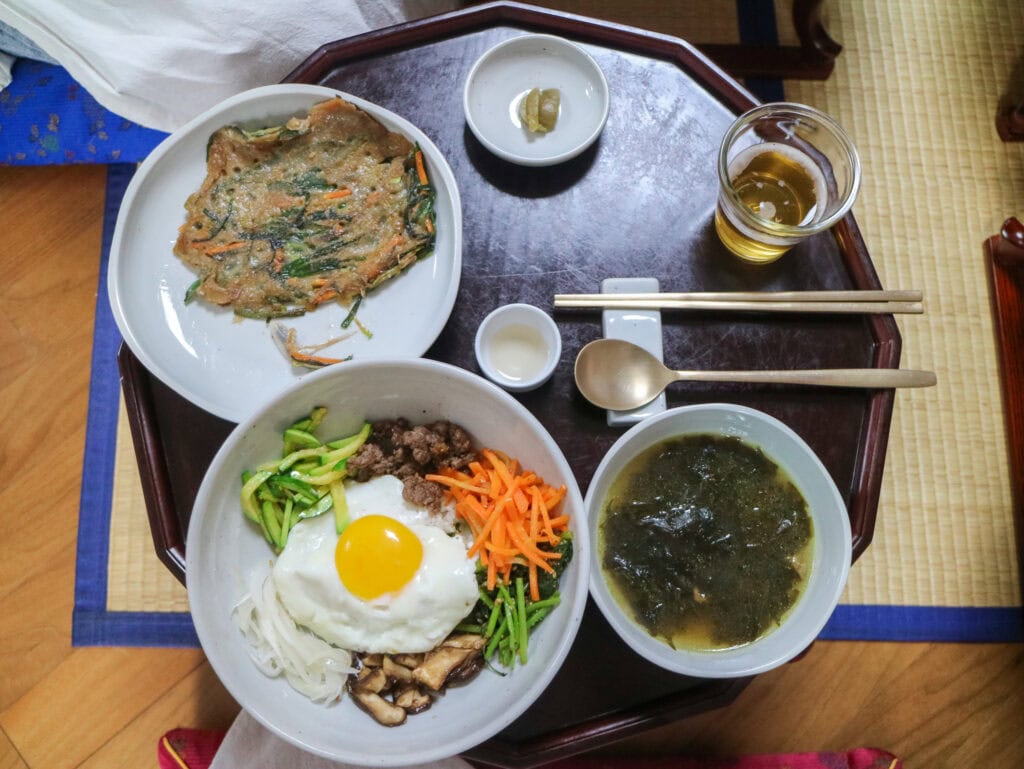 Traditional Korean meal with bibimbap, soup, and side dishes on a tray.