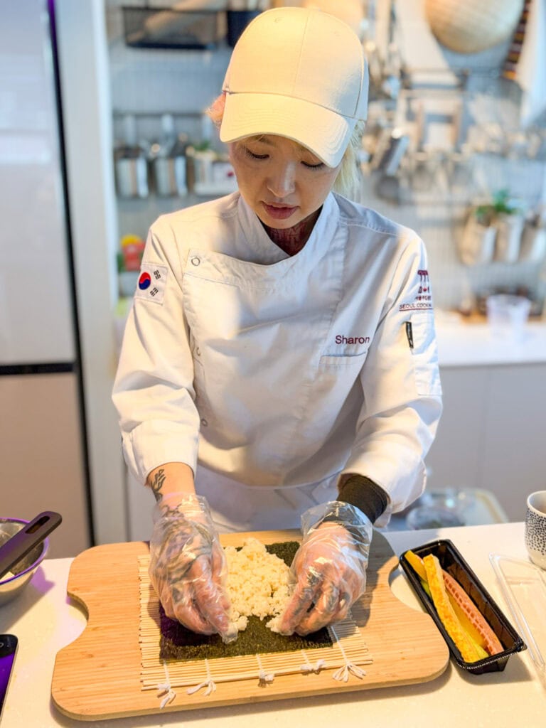 Korean chef preparing sushi roll in a professional kitchen.