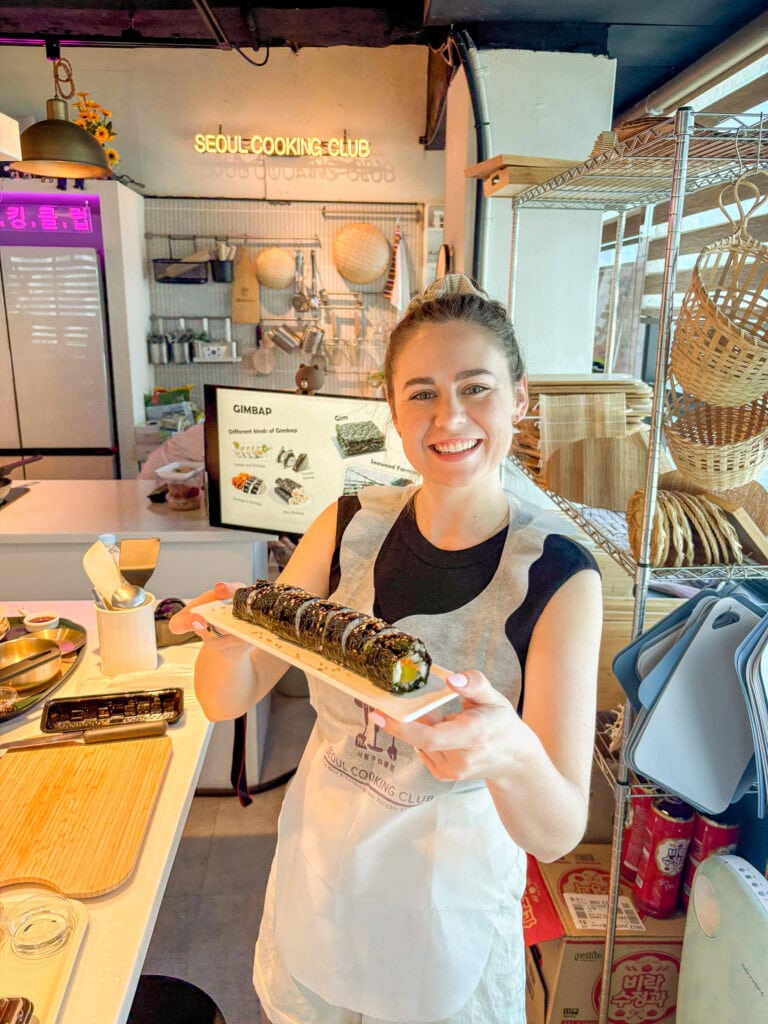 Smiling woman holding a plate of sushi at Seoul Cooking Club in Seoul.