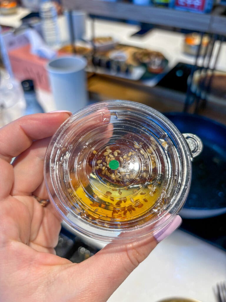 Close-up of a hand holding a small clear cup with golden liquid and sesame seeds.