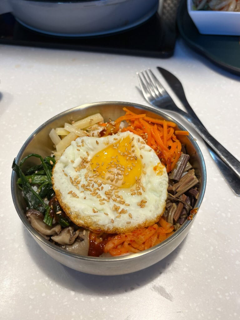 Korean bibimbap with fried egg, vegetables, and rice in a bowl.