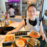 Happy woman holding a tray of Korean dishes at Seoul Cooking Club in Seoul.