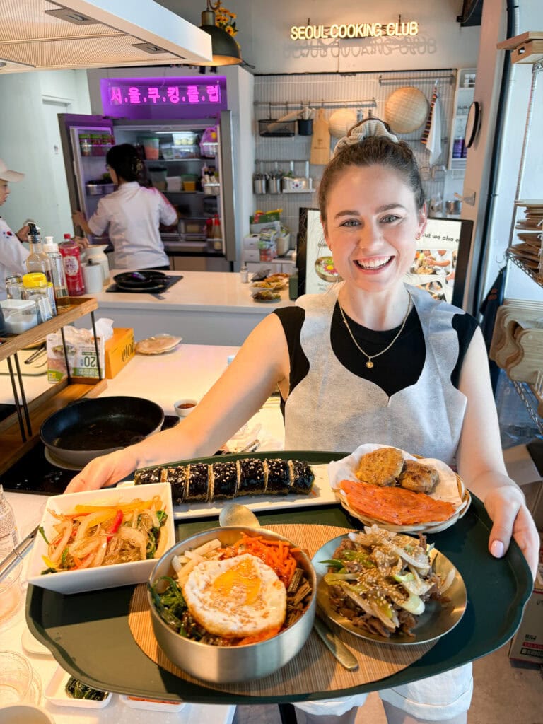 Happy woman holding a tray of Korean dishes at Seoul Cooking Club in Seoul.