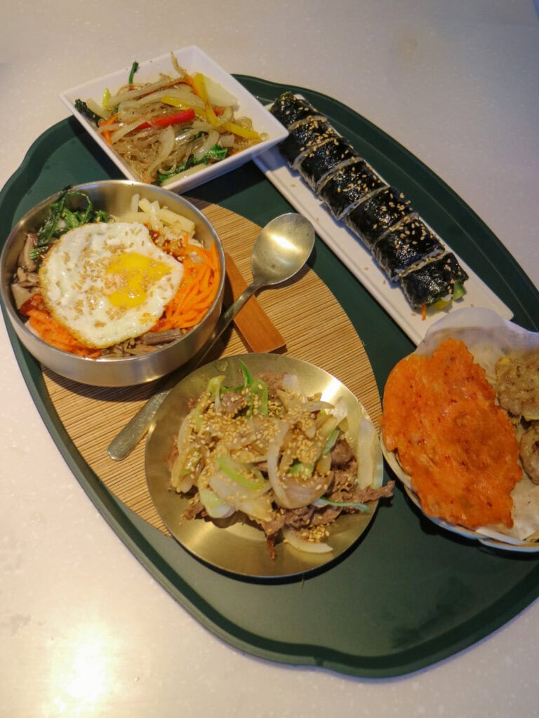 Assorted Korean dishes including kimbap, bibimbap, and side dishes on a tray.