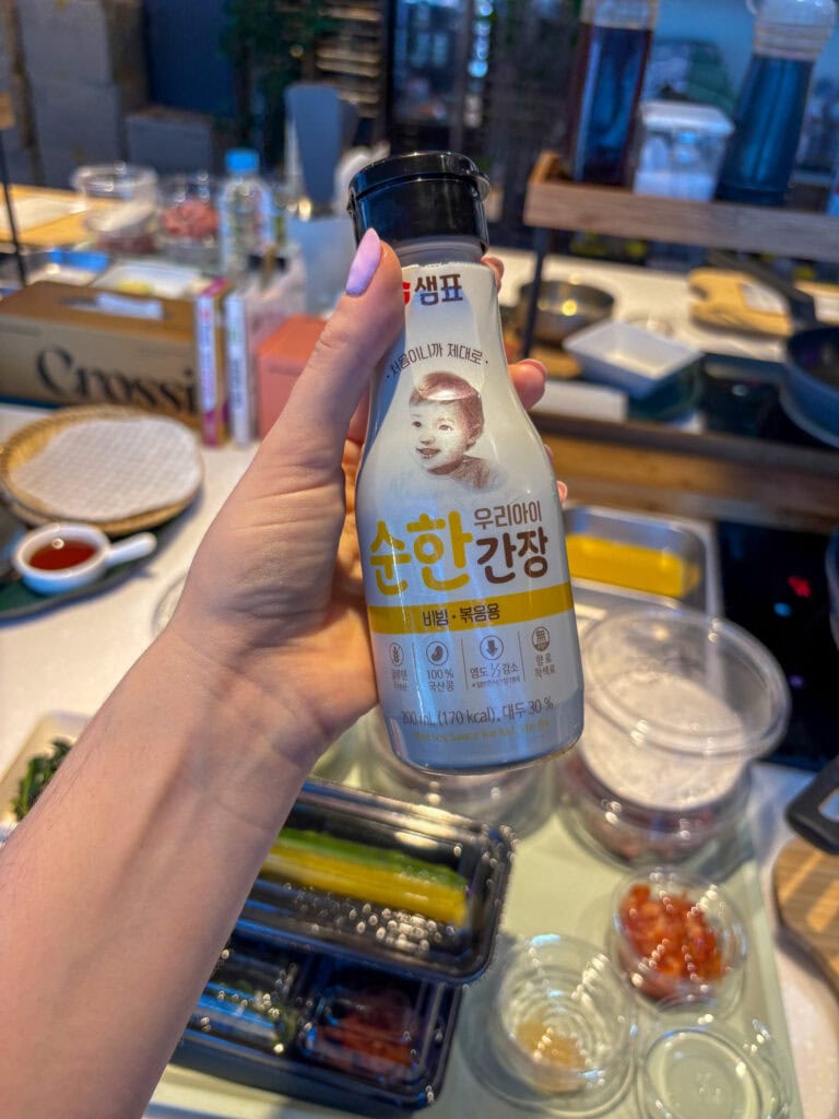 Korean soy sauce in a hand with a busy kitchen background.